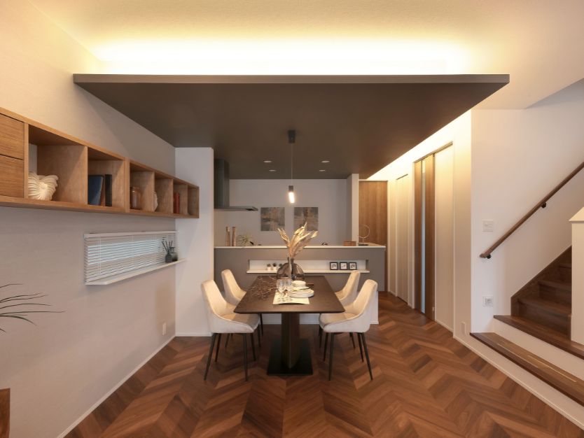 ヘリンボーンの床が特徴的なリビングダイニング。手前に黒いソファとローテーブル、奥にグレーの下がり天井があるダイニングスペース。