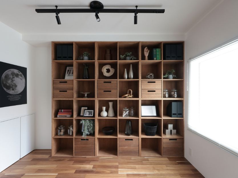 大きな木製シェルフとデスクスペースがあるリビングルーム。黒いソファと低い仕切り壁が空間を分けている。