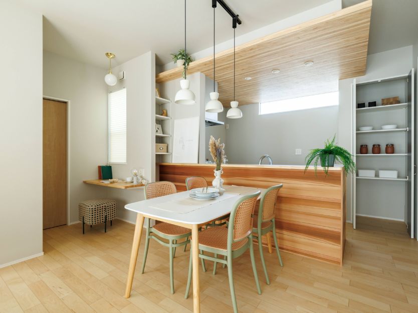 ナチュラルな内装のリビングダイニング全体。手前にベージュのソファと円形ラグ、奥にダイニングキッチンが見える。