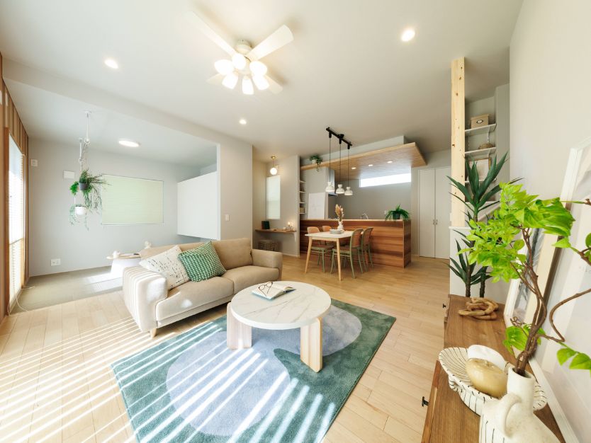 ナチュラルな内装のリビングダイニング全体。手前にベージュのソファと円形ラグ、奥にダイニングキッチンが見える。